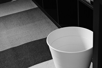Grayscale shot of a white bucket on the carpet in a kitchen