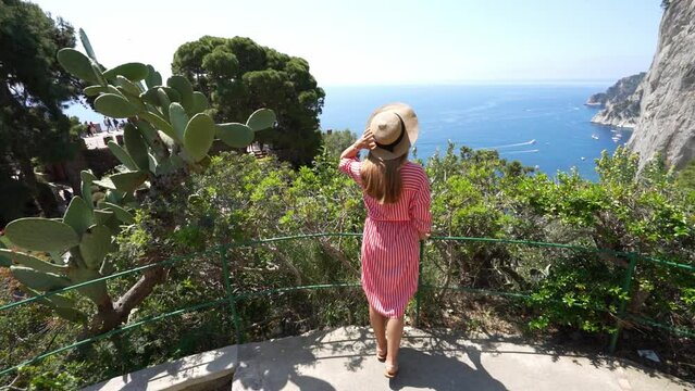 Beautiful young woman with hat sitting on wall looking at stunning panoramic village of Atrani on Amalfi Coast, Italy