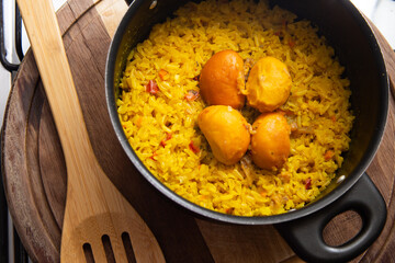 Uma panela preta com arroz com pequi e uma colher de madeira, sobre uma tábua de cozinha. Um prato típico brasileiro.