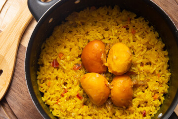 Uma panela preta com arroz com pequi e uma colher de madeira, sobre uma tábua de cozinha. Um prato típico brasileiro.