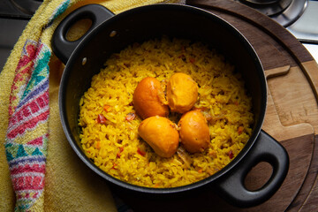 Uma panela preta com arroz e pequi sobre uma tábua de madeira e um pano de prato. Um prato típico brasileiro.