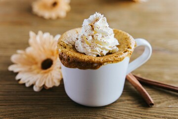 Selective focus shot of Pumpkin Spiced mug cake with cinnamon sticks and flower on wooden table