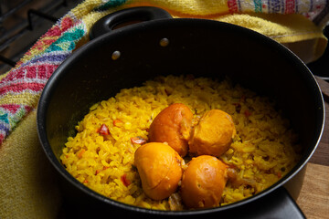 Uma panela preta com arroz e pequi sobre uma tábua de madeira e um pano de prato. Um prato típico brasileiro.