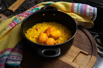 Uma panela preta com arroz e pequi sobre uma tábua de madeira e um pano de prato. Um prato típico brasileiro.