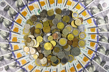 A bunch of different coins from around the world on the background of one hundred dollar bills of American dollars laid out in a circle