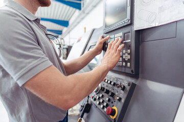 Fototapeta na wymiar Manufacturing worker programming industrial CNC machine tool while entering work data