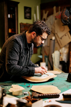 Portrait of leather craftsman makes a leather motorcycle seat at table in workshop studio