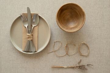Home decor, natural style, eco friendly lifestyle concept. Ceramic plate, set of metal cutlery fastened with string lying on paper napkin, dry lavender, eco inscription on brown tablecloth.Copy  space
