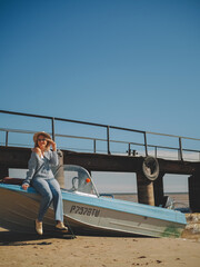 Portrait of a young beautiful girl in a blue sweater and jeans is on a boat near the river pier