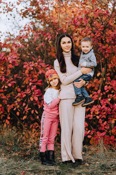 Photography, portrait of a beautiful girl, woman with a little son and daughter in nature in autumn, against the backdrop of a tree with red leaves.