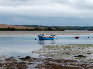 Clonakilty Bay at low tide. A small blue fishing boat is anchored. Open seabed, silt and algae. Picturesque seaside landscape.