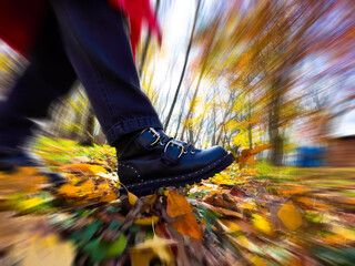 Female legs in boots on autumn leaves. Kicking dry leaves in park with motion blur effect