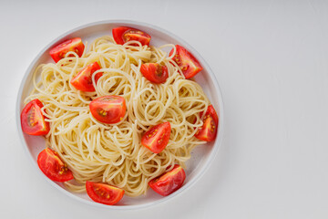 Spaghetti plate with cherry tomato slices on white background. Italian pasta and red tomatoes on a white plate. Top view. Copy space