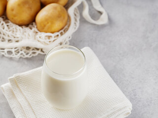 Potato milk and raw potatoes in a mesh bag. Alternative non dairy drink and ingredients on gray background. Allergens free and zero waste concept. Top view. Copy space