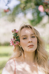 Portrait of a beautiful girl looking directly at the camera, blooming apple orchard, long blond hair, spring time