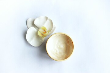 Fototapeta na wymiar A white orchid flower and a jar of cosmetic cream on a white background. View from above. Cosmetic products.
