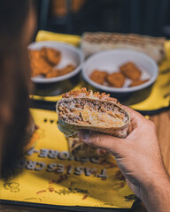 Tacos viande hachée tenu dans la main droite d'un homme barbu sur fond de nuggets et tenders