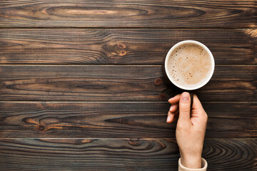 Minimalistic style woman hand holding a cup of coffee on Colored background. Flat lay, top view cappuccino cup. Empty place for text, copy space. Coffee addiction. Top view, flat lay