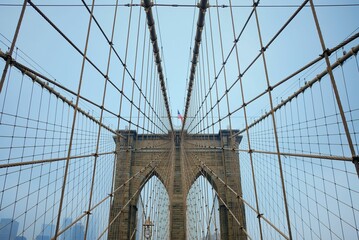 Low angle shot of American flag flying on top Brooklyn Bridge in New York City USA under blue sky