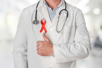 Doctor wearing a red ribbon on his chest, symbol of World AIDS Day, and raising his thumb in...