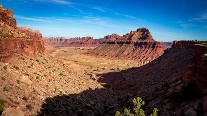 Scenic shot of a red desert valley with cliffs and peaks with the blue sky in the background