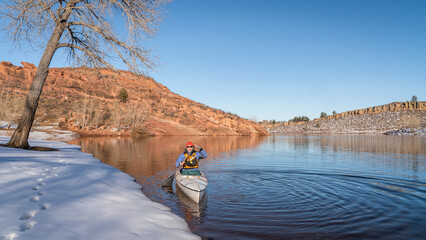 senior male wearing life jacket is paddling expedition canoe in winter scenery of Horsetooth...