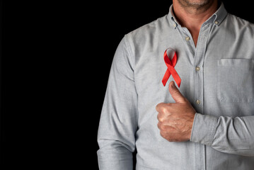 A man wearing a red World AIDS Day ribbon on his chest with his thumb up in support of all HIV positive people. Fighting the hiv virus. Respect and understanding for people living with AIDS