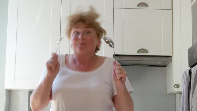 body positive blond middle-aged woman dancing in kitchen with frying pan and ladle, emotion image, cooking love concept