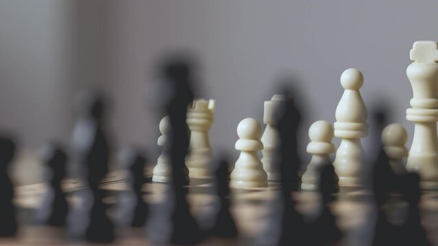 Close up and slow motion planning of chess pieces in row with blurred foreground of black chess enemy shows concept of competition with strategic business planning of teamwork for winning the battle.