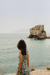 Vertical of a girl in a cute dress standing toward the sea at the beach