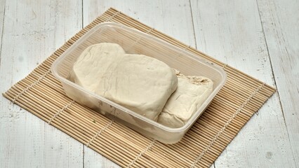 High-angle shot of raw tofu pieces on a plastic container on a wooden mat