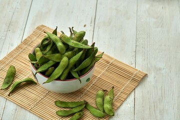 High-angle shot of a bunch of edamame in a bowl on a wooden mat