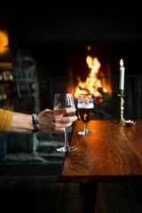 Human hand holding glass of wine by wooden table with blur fireplace in the background