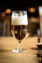 Vertical shot of a glass of foamy beer on wooden restaurant table