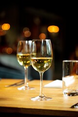 Vertical selective focus shot of glass of white wine on wooden restaurant table on bokeh background
