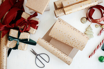 Wrapping stylish christmas gift flat lay. Modern gift boxes, red and green ribbons, golden wrapping paper, ornaments and scissors on white background. Merry Christmas! Atmospheric winter time