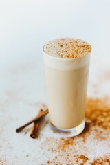 Closeup shot of a glass of a cinnamon mocha shake, surrounded with cinnamon sticks and powder