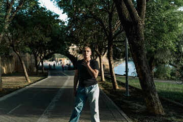 Fototapeta na wymiar Young non-binary person of South American origin looking at camera while posing standing in the middle of a city street. LGBTIQ concept.