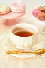 Teacup on a saucer with a gold-plated spoon alongside macarons and donuts