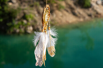 Close up dream catcher hanging over the azure lake, bohemian craft outdoors