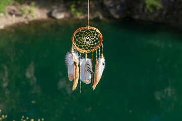 Close up dream catcher hanging over the azure lake, bohemian craft outdoors