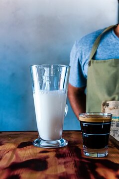 Vertical shot of cup of coffee and other with milk on wooden table and a person standing