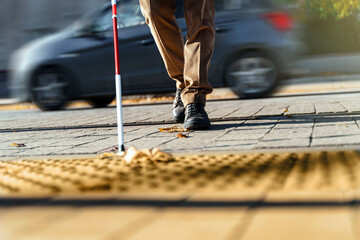 Blind man close-up with a walking stick crosses the road in front of a passing car