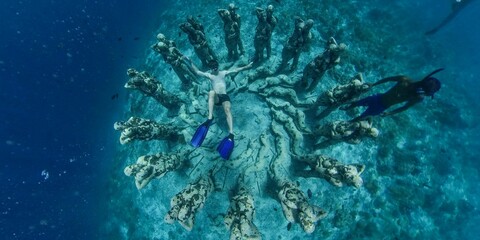 Underwater scenery with sunk old sculptures covered in moss and people scuba diving