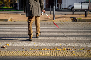 Blind man close-up with a walking stick crosses the road across the pedestrian crossing