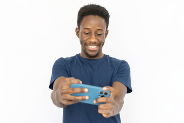 Happy man holding smartphone with both hands. Young African American male model in blue T-shirt playing mobile game or watching video. Portrait, studio shot, technology, joy concept
