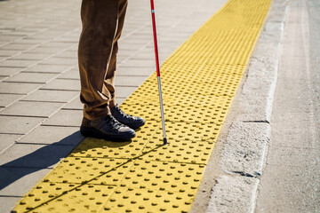 Close-up of a blind man with a walking stick. Stands on a tactile tile for self-orientation while...