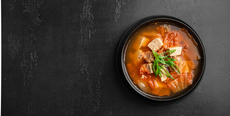 Korean food, kimchi soup with tofu in a ceramic bowl on a black background, top view, copy space