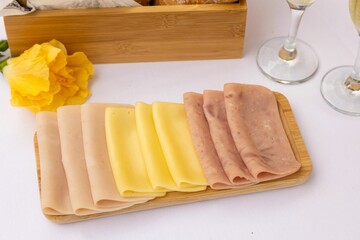 Top closeup of slices of ham and cheese on the wooden narrow and long plate on white background