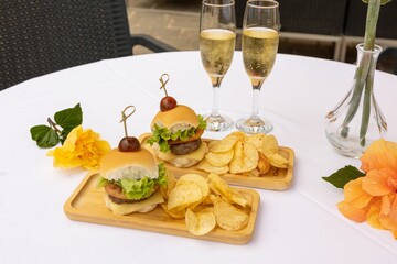 Top closeup of burger and chips on the wooden plates, two glasses full of champagne
